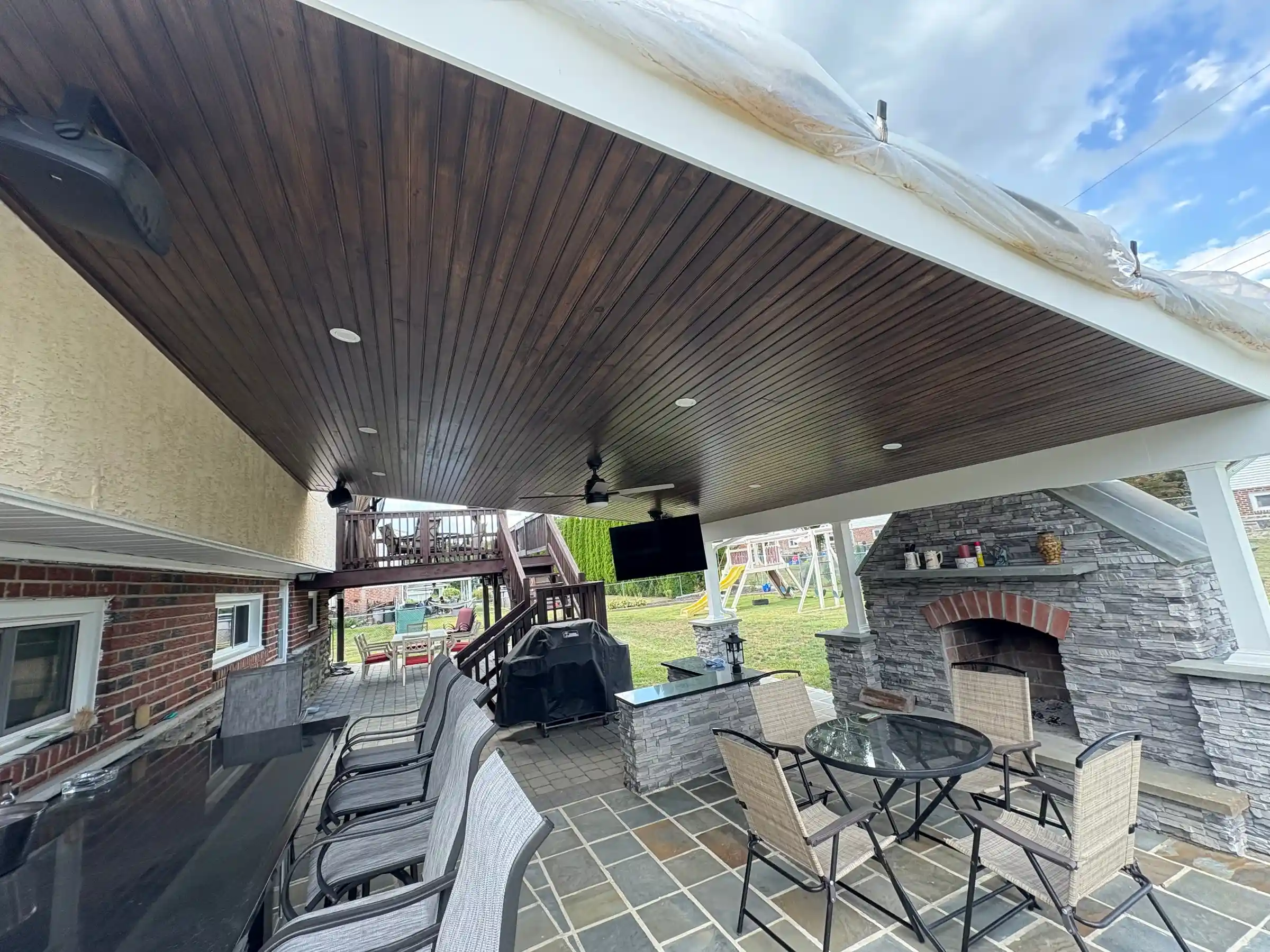 Covered outdoor patio with painted wood ceiling and stone fireplace