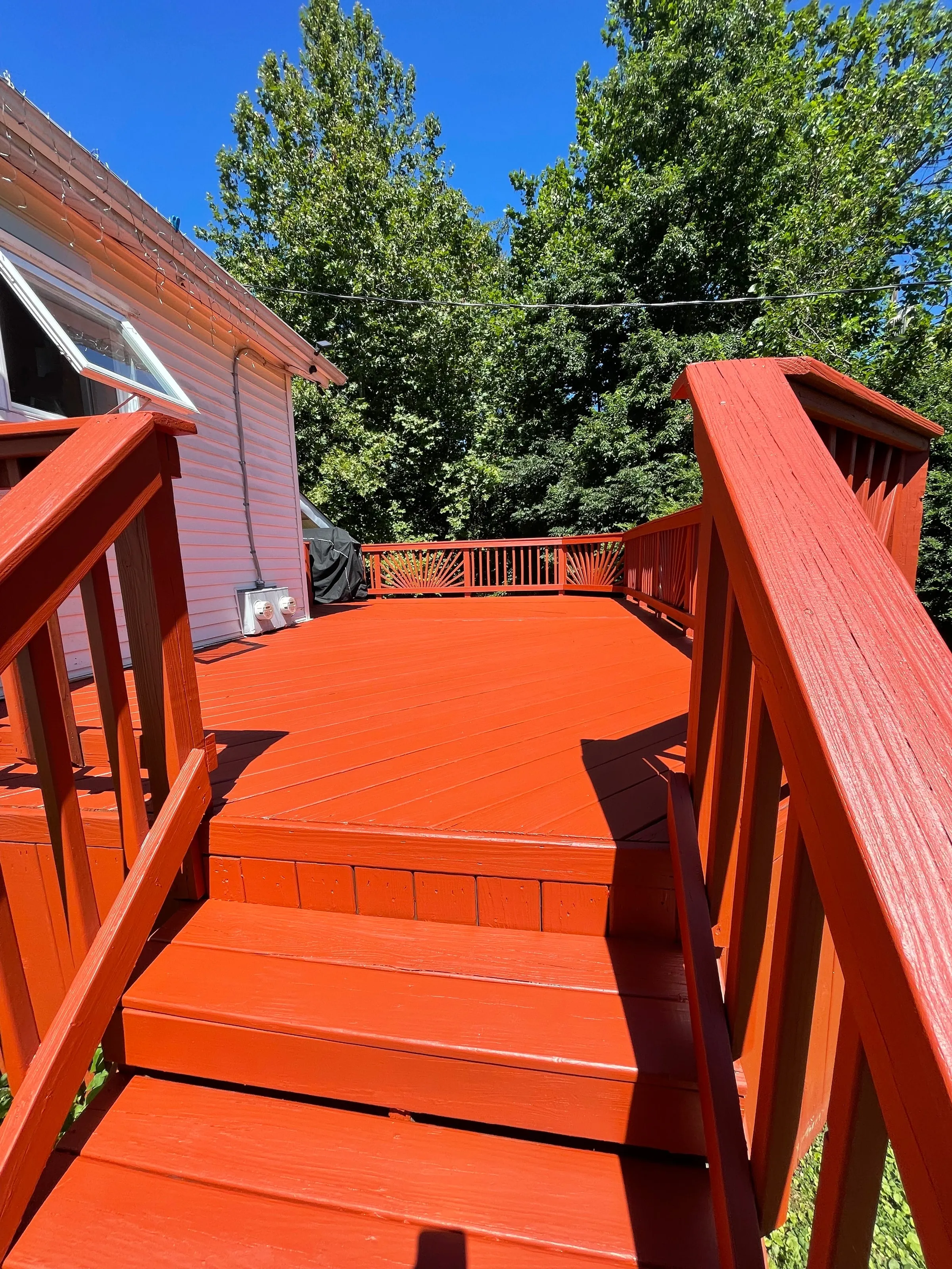 Deck stairs and railings finished in a solid red stain against a blue sky