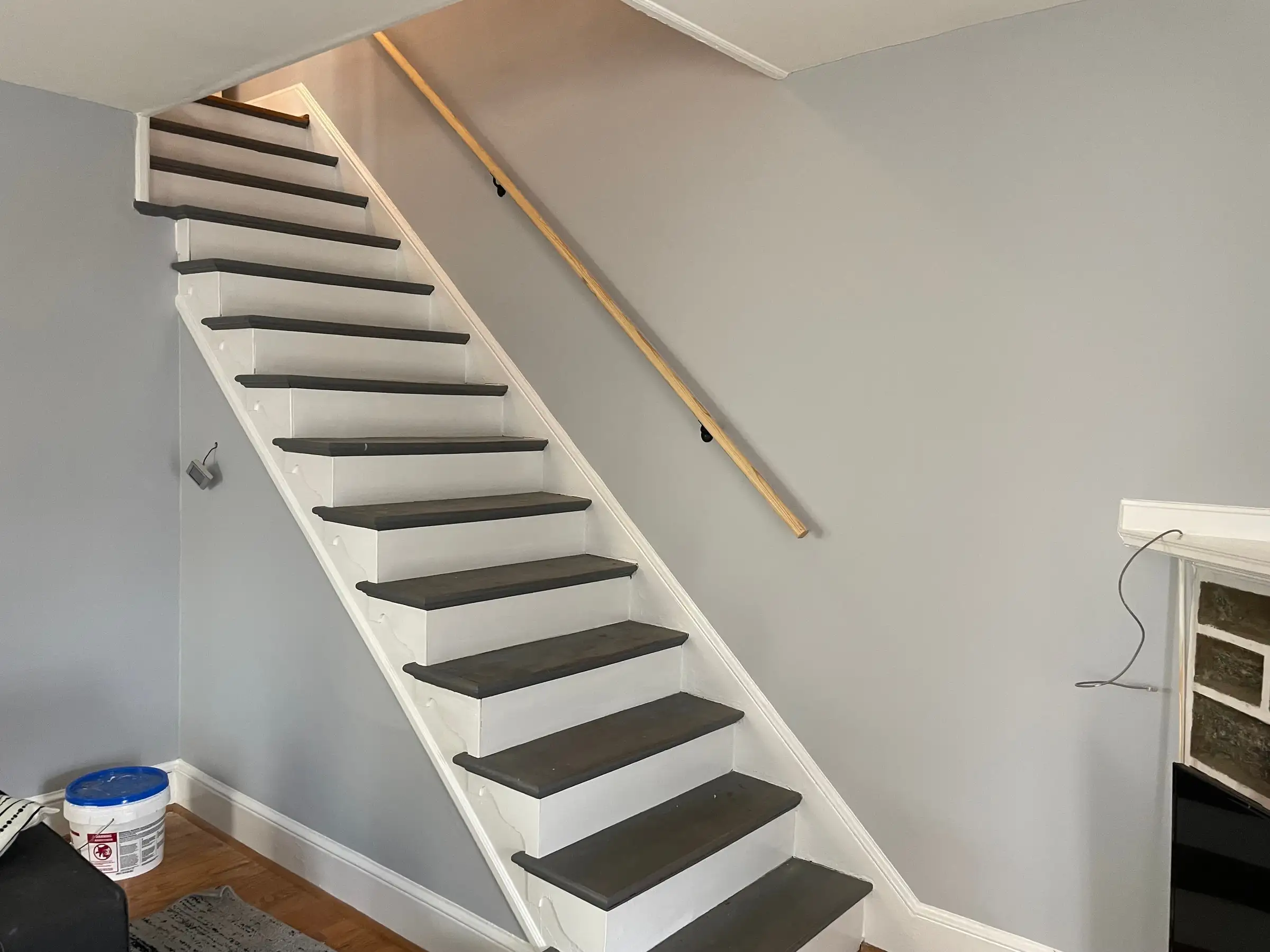 Interior staircase painted white with a wood handrail, mid-project